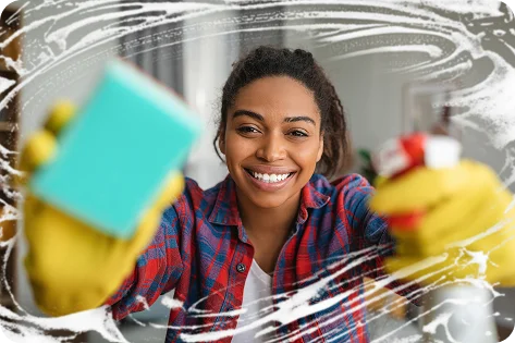 Une personne souriante vêtue d'une chemise à carreaux et de gants jaunes tient une éponge et un vaporisateur, nettoyant une fenêtre avec de la mousse savonneuse qui encadre les bords. Lumineux et joyeux